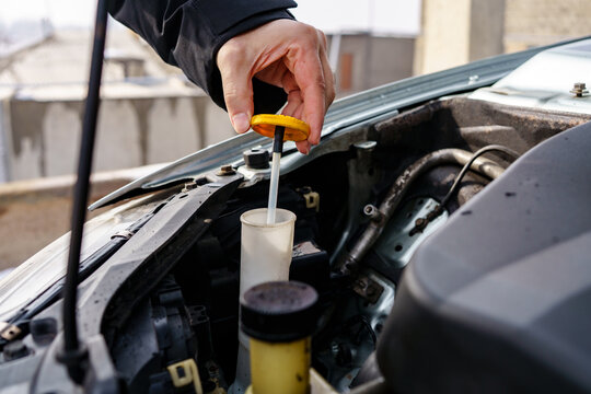 A close-up of a mechanic's hand opening a yellow cap with a dipstick from the windshield washer fluid reservoir under a car hood.