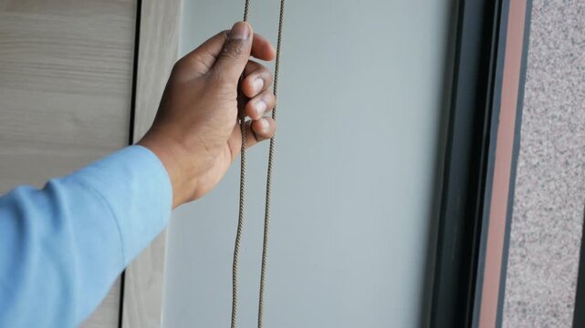 Person closing roller window blinds using a chain mechanism inside modern office or apartment interior