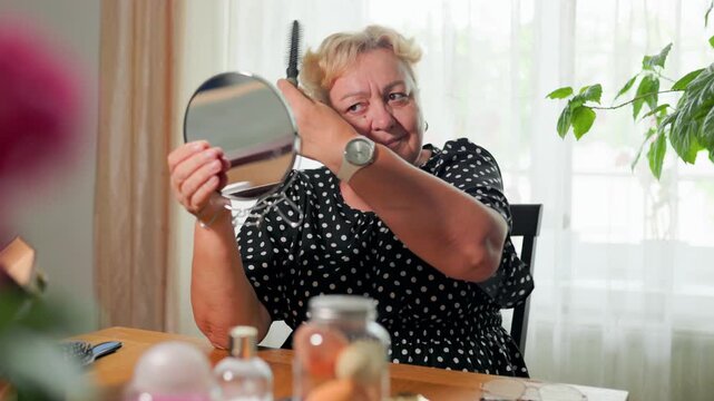 Elderly woman brushing hair and evaluating physical appearance at home