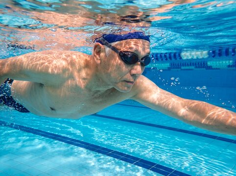 senior man swimming pool underwater fitness athlete endurance retirement wellness A swimmer glides through water during lap training showing vitality discipline and healthy aging for sports campaigns