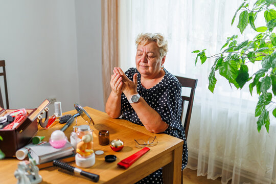 Mature female massaging skincare lotion into her hands during daytime.