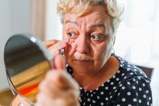 Macro close up of mature older woman examining under eye wrinkles.