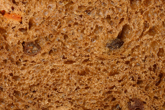 The texture of a porous slice of rye bread with raisins and dried apricots