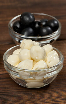 Mozzarella balls in a glass bowl in the foreground, blurred olives