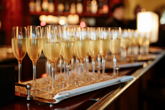 Row of champagne flutes filled with sparkling wine on a silver tray, captured in a dim, atmospheric bar setting perfect for events and nightlife, celebrating festivities, events, toast