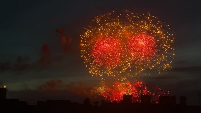 Bright orange fireworks exploding in night sky above silhouette of city skyline. Festive pyrotechnic display during Independence Day celebration. Event concept and national holiday.