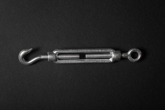 Steel turnbuckle for tightening wire for grape trellis on black background.