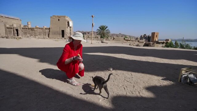 A woman in a red dress exploring the ruins of the Philae Temple, Aswan, Egypt.