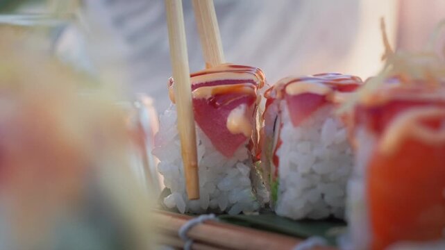 Macro handheld slow motion footage of chopsticks lifting a fresh salmon sushi roll from a plate, highlighting rice texture, sauce and soft restaurant lighting.