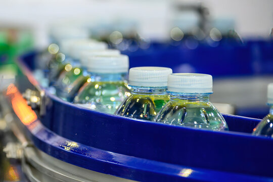 Macro shot of filled drinking water bottles moving on an automated conveyor belt in a bottling plant.