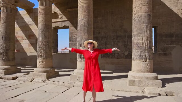 A woman in a red dress exploring the ruins of the Philae Temple, Aswan, Egypt.
