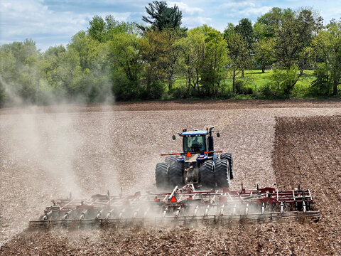 Blue tractor pulling a red field cultivator to prep the field for spring planting.