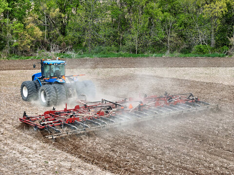 Blue tractor pulling a red field cultivator to prep the field for spring planting.