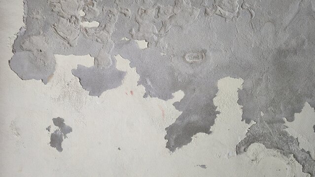 Old cement wall with peeling paint and cracked plaster texture. Weathered concrete surface with flaking wall paint, showcasing a rugged distressed texture layers.