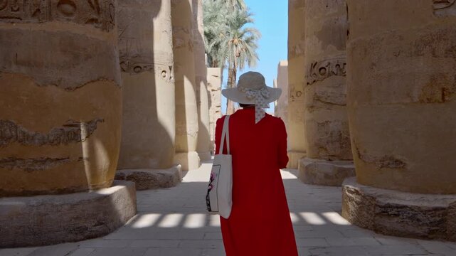 A woman in a red dress exploring the ruins of the Karnak Temple, Luxor, Egypt.