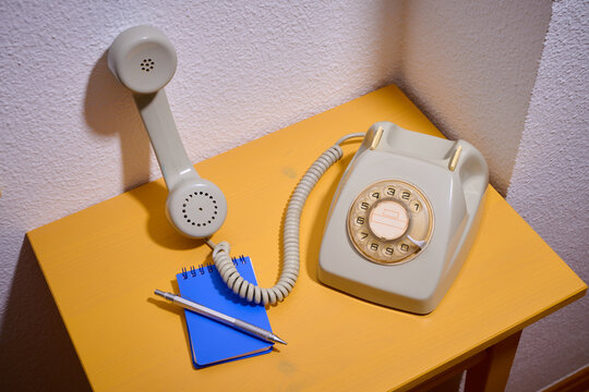 Close-up of an old rotary dial telephone on a yellow wooden table and a small notepad.