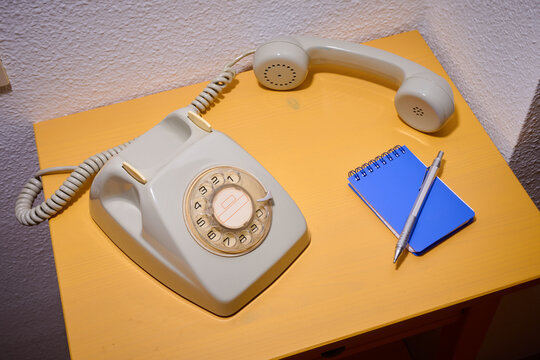 Close-up of an old rotary dial telephone on a yellow wooden table and a small notepad.