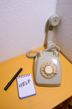 Close-up of an old rotary phone on a yellow wooden table and a small notepad with the word help written on it.