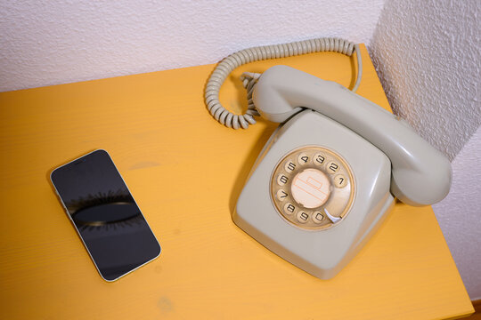 Close-up of an old rotary phone and a modern smartphone on a yellow wooden table.