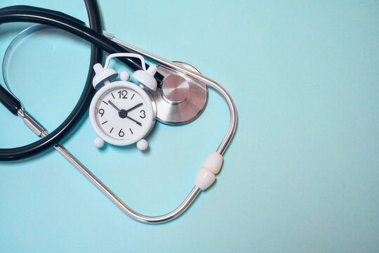 Medical stethoscope and small alarm clock on a blue background
