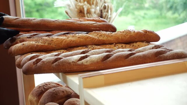 Close-up of a pastry chef putting a freshly baked baguette on a shelf in a store or bakery. Delicious bread. The concept of public catering.