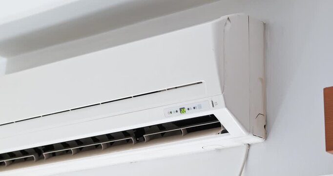 Wall-mounted air conditioner unit with moving flap in operation blowing cool air into a room during a hot summer afternoon