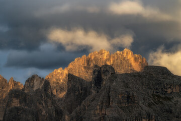 Dramatic mountain peaks illuminated by golden hour sunlight under a heavy, stormy sky. Perfect for travel, nature, and adventure themes. © marcodenaro