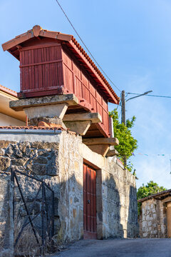 Traditional red wooden horreo granary built on a stone wall in a village of Galicia, Spain.