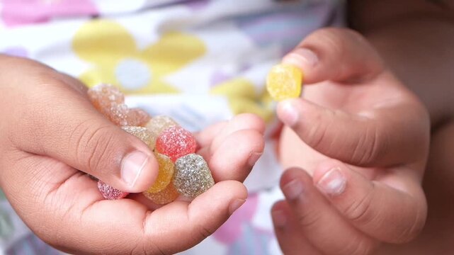 Child holding colorful sugar coated gummy candies in palm of hands while playing with a yellow piece in slow motion