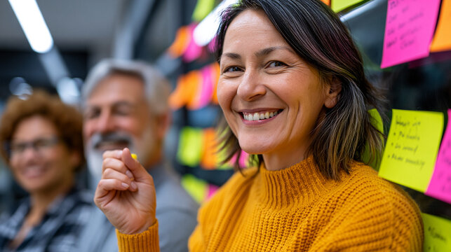 Diversity program manager facilitates a workshop where employees from multiple departments write responses on individual index cards that they then post to a large shared wall display, warm room lig