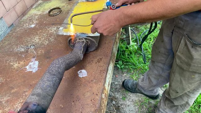 Mechanic gas welding a rusty car exhaust pipe outdoors