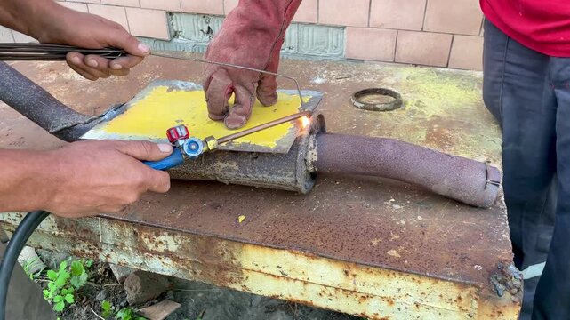 Two mechanics repairing and gas welding rusty car exhaust pipe outdoors