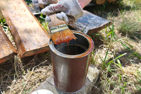Applying wood stain with a paintbrush to a wooden surface outdoors. Close-up of DIY woodworking, timber treatment, renovation and protective finishing.