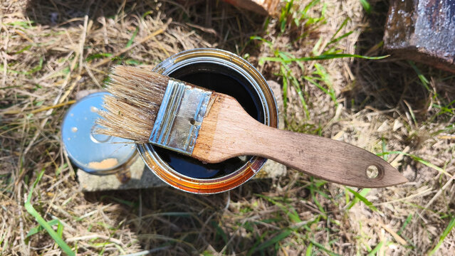 Open can of wood stain with paintbrush resting on top outdoors. Wood finishing materials, DIY renovation, woodworking supplies and timber protection concept.