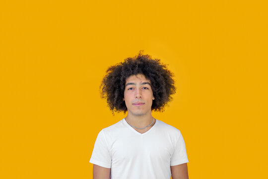 Portrait beautiful men of mixed race african-Italian on a yellow background. A young ethnic man with curly hair in a white t-shirt looks positive, relaxed