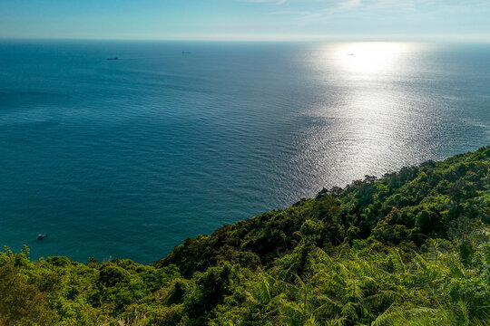 Lush forest slopes stretch toward the deep blue sea at Son Tra Peninsula as sunlight reflects off the water on a clear afternoon in beautiful coastal Danang Vietnam