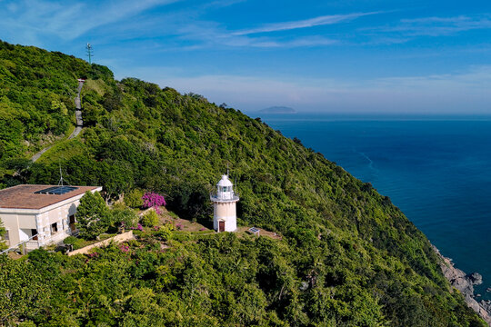 Lighthouse stands on a lush green cliff surrounded by jungle forest overlooking the deep blue sea on Son Tra Peninsula in Danang on a clear morning