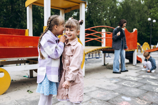 Little positive girls whispering secrets and sharing joy on playground