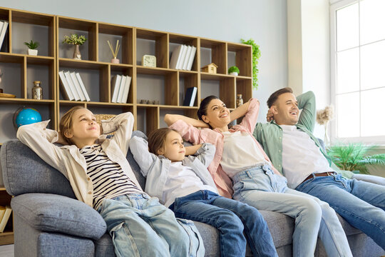 Family parents children on sofa relaxing home together. Bright living room shows bonding and cozy comfort, ideal for ads on home lifestyle and insurance. Theme of family unity and comfort.