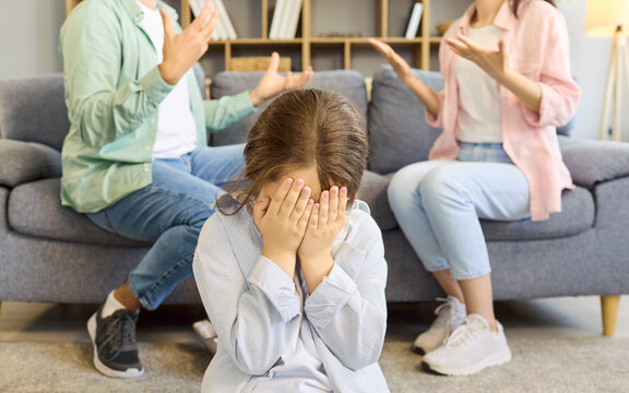 Child parents family conflict argument triggers anxiety. Girl hides face while adults shout on sofa, portraying domestic tension and fear at home. Powerful concept of family stress and trauma.