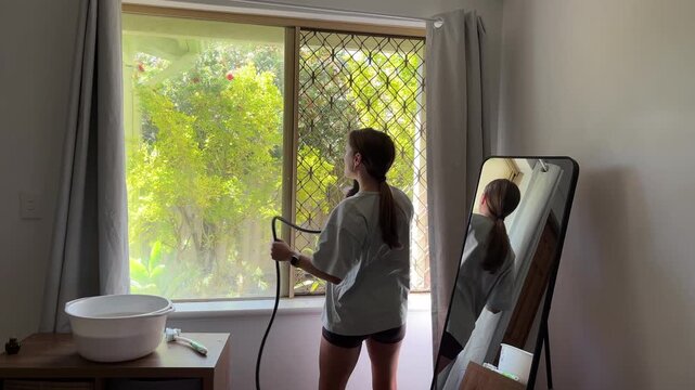 A woman is dancing in a bright room with sunlight coming through the window. She appears happy and carefree as she moves.