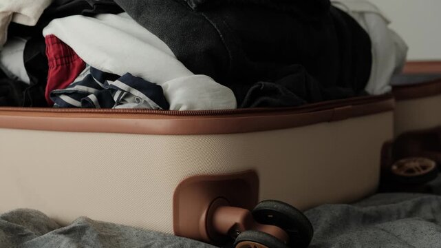 Close up of hands opening an overpacked suitcase with poorly organized clothes after unsuccessful packing attempt before travel or relocation