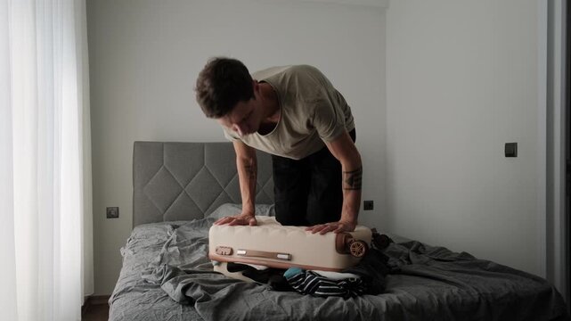 Overpacked suitcase and packing stress. Man struggling to close overloaded luggage before travel or relocation, showing common packing mistakes and authentic lifestyle
