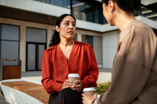 Two businesswomen talking over coffee outside an office building