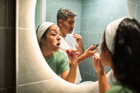 Couple brushing teeth together at home bathroom mirror