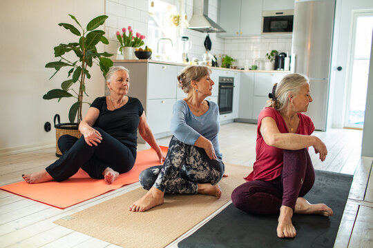 Three senior women doing seated yoga stretches at home kitchen