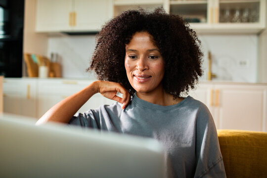 Smiling woman working on laptop in home kitchen