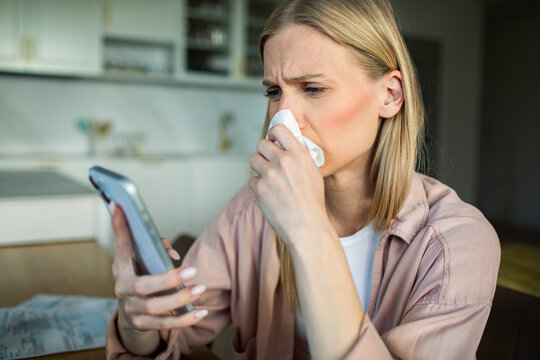 Sick woman checking symptoms on smartphone in home kitchen