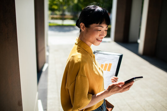 Smiling businesswoman checking smartphone outside office