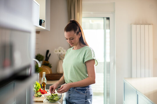 Young woman preparing fresh salad in home kitchen